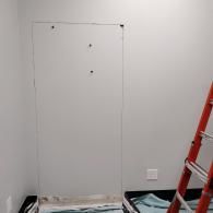 A rectangular outline drawn on a light gray wall next to a red ladder, indicating a space marked for cutting or access.