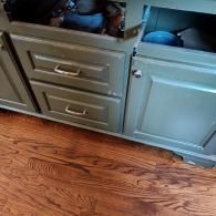 A light green cabinet featuring two stacked drawers and a small open storage section, set atop hardwood flooring.