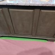 A dark-brown wooden cabinet with three recessed panel doors sitting below a light-colored granite countertop.