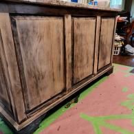 A kitchen island with a granite countertop and cabinets featuring a weathered, distressed light and dark wood finish.