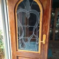 A wooden front door with an arched glass panel featuring a decorative, flowing etched-glass design.