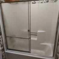 A white fiberglass shower-tub combination featuring sliding glass doors with a metal frame.