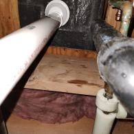 Close-up of white and black PVC plumbing pipes running through a wooden structure with pink insulation below.