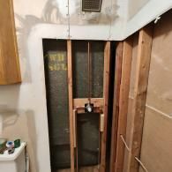 A partially renovated bathroom shower area featuring exposed wooden wall studs and copper plumbing pipes.