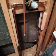 Copper pipes and a plumbing valve assembly installed between wooden wall studs inside a home.