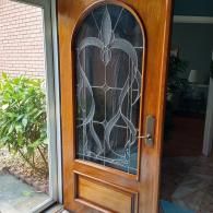 A wooden front door with an arched glass panel featuring a decorative leaded design, seen from an entryway.