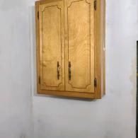 A light wood-toned, two-door wall cabinet mounted on a plain white wall.