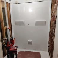 A white shower stall surround installed in a bathroom frame with visible wall studs and tools in the foreground.