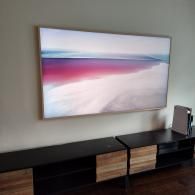 A wall-mounted TV displaying a serene pink and blue landscape, placed above a modern black and light wood media console.