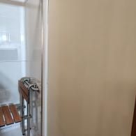 A wall-mounted, fold-down wooden shower seat with a metal safety grab bar inside a white shower stall.