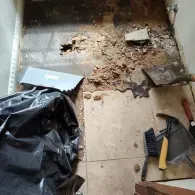 Renovation of a tiled floor with debris, a trowel, a hammer, and a plastic trash bag on the ground.