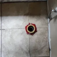 A top-down view of a toilet drain flange with a wax ring on a tiled floor, ready for toilet installation.