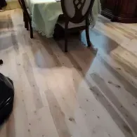 Light-colored wood flooring in a dining area, featuring a table with a pale cloth and a dark wooden chair.