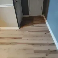 Light-colored wood-look flooring installed in a hallway with white door frames and blue-gray walls.