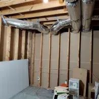 Unfinished basement with exposed wooden studs, silver HVAC ductwork, and some scattered building materials.