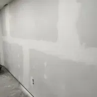 A wall under construction featuring drywall panels with seams covered in tape and compound, with an electrical outlet.