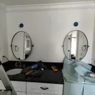 A bathroom vanity under construction with two oval mirrors, a black countertop, and two light fixtures waiting for covers.
