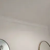 A white ceiling with decorative crown molding and portions of two circular mirrors visible at the bottom.