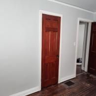 A light gray hallway with a six-panel wood-stained door, white trim, and dark hardwood floors.