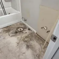 An unfinished bathroom renovation with a bare concrete floor, a drain, and exposed plumbing pipes on the wall.