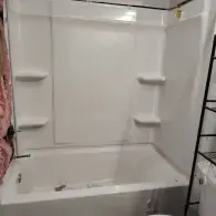 A white bathtub and shower surround with built-in shelves, viewed from an angle in a bathroom.