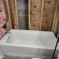 A white bathtub installed in a bathroom alcove with exposed wall studs and pink fiberglass insulation.
