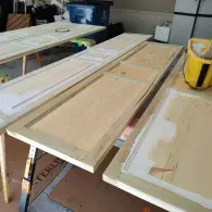 Several unfinished wooden doors are laid out across sawhorses in a garage for painting or renovation.