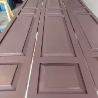 Three brown, freshly painted wooden doors with rectangular panels laid out side-by-side.