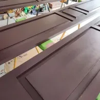 Several rectangular wooden door panels painted a matte brown finish, resting on yellow sawhorses.