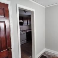 A view through a doorway into a kitchen with dark wooden cabinets, white appliances, and gray walls.