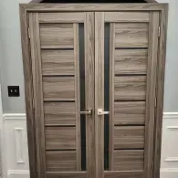 Double doors featuring horizontal wood panels and a vertical glass insert in a grey, wood-grain finish.