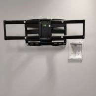 A black, articulating TV wall mount attached to a white wall next to a recessed cable management and power box.