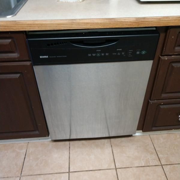 A stainless steel dishwasher with a black control panel built into dark brown kitchen cabinetry.