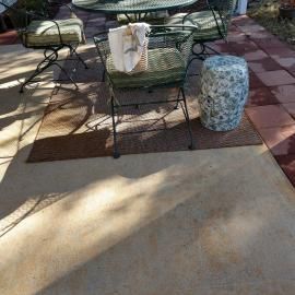 A metal patio furniture set with cushions and a floral ceramic stool on a paved deck under dappled sunlight.