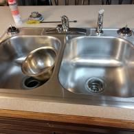 A stainless steel double-basin kitchen sink set in a countertop with a faucet and a metal mixing bowl inside the left basin.