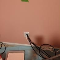 A wall outlet with several black power cords plugged in, situated above a paint tray on a blue drop cloth.
