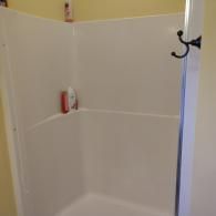 A white fiberglass shower stall in a bathroom with a black double-hook attached to the frame.