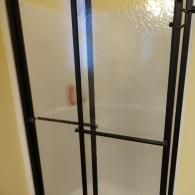 A shower stall with textured glass panels, a black metal frame, and a horizontal handle bar.