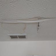 A water-damaged ceiling featuring a long, sagging area of drywall with brown staining and loose, hanging wires.