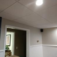 A view of an interior room featuring a drop ceiling, beige walls with white wainscoting, and an open doorway to another room.