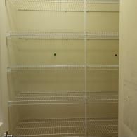 A pantry closet featuring five empty white wire shelves mounted against a plain, light-colored wall.