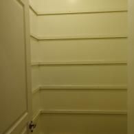 A small, empty pantry with white walls and four evenly spaced white wooden shelves.