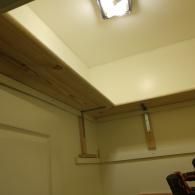 Wooden shelves installed in the corner of a room, supported by white brackets against off-white walls.