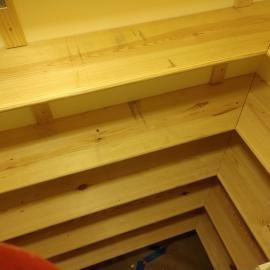 Light-colored, unfinished wooden shelves installed in a corner, showing a multi-tiered staircase-like layout.