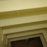 A close-up, angled view of off-white, tiered shelving mounted against a plain wall.