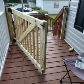 A wooden gate stands partially open on a deck, with steps leading down to a driveway in the background.