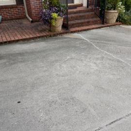 A gray concrete driveway leads to brick stairs with a decorative planter in front of a brick building.