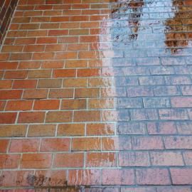 A brick surface showing a sharp contrast between a dry, orange-red section and a wet, dark, reflective section.