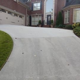 A wide concrete driveway leading to the garage and front entrance of a multi-story brick house with a green lawn.