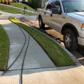 A silver pickup truck parked on a residential street with a long electrical cord running across the sidewalk.